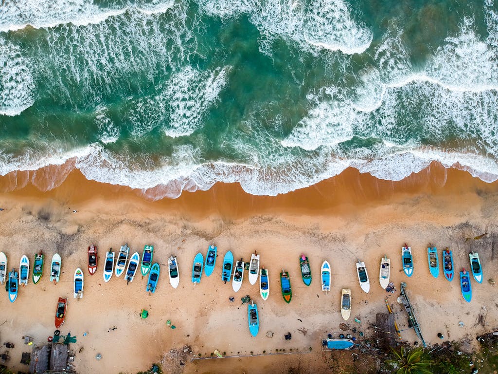 Stunning aerial shot of vibrant boats lined on sandy shores of Arugam Bay, Sri Lanka.